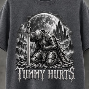 Könnte beinhalten: Ein dunkelgraues T-Shirt mit einem Grafikdruck eines Ritters in voller Rüstung, der auf felsigem Boden kniet und ein Schwert hält. Im Hintergrund leuchtet ein großer Vollmond hinter einer gotischen Burg. Der Text "TUMMY HURTS" ist darunter gedruckt.