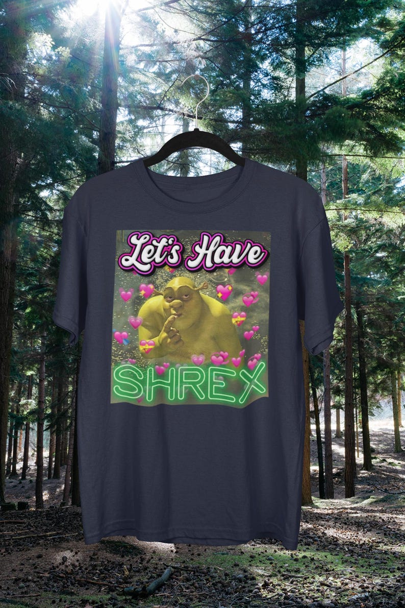 May include: A dark blue t-shirt with a green ogre character from the movie Shrek. The text "Let's Have Shrek" is printed on the shirt in a pink and white font.