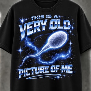 May include: A black short-sleeve t-shirt featuring a graphic of a sperm cell surrounded by blue lightning and stars. The text reads THIS IS A VERY OLD PICTURE OF ME in a metallic blue font. The design is centered on the front of the garment.