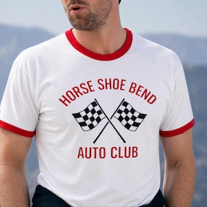 May include: White ringer t-shirt with red trim. The shirt displays the text "HORSE SHOE BEND AUTO CLUB" in red, and two crossed checkered flags. A classic design.