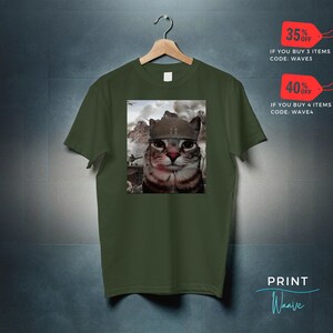 May include: A green t-shirt with a print of a cat wearing a military helmet. The cat is looking directly at the viewer. The background of the print is a blurry image of a war scene. The t-shirt is hanging on a hanger. The text "35% OFF" and "IF YOU BUY 3 ITEMS CODE: WAVE3" is in the top right corner of the image. The text "40% OFF" and "IF YOU BUY 4 ITEMS CODE: WAVE4" is in the bottom right corner of the image. The text "PRINT Waave" is in the bottom right corner of the image.