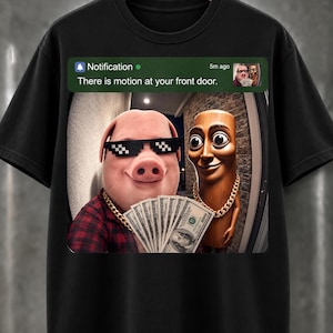Puede incluir: Una camiseta negra con un estampado gráfico de una notificación de smartphone que dice "Notification 5m ago There is motion at your front door." La imagen muestra un cerdo con gafas de sol pixeladas y una cadena de oro sosteniendo dinero.