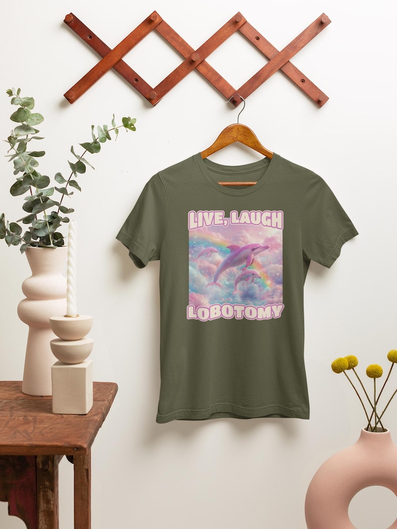 May include: A green t-shirt with a pink dolphin jumping over a rainbow in a cloud. The text "LIVE, LAUGH LOBOTOMY" is printed on the shirt.