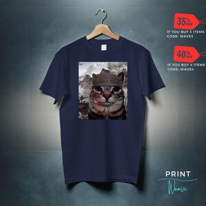May include: A navy blue t-shirt with a graphic of a cat wearing a military helmet. The cat is looking directly at the viewer. The background of the graphic is a war scene. The text "35% OFF IF YOU BUY 3 ITEMS CODE: WAVE3" and "40% OFF IF YOU BUY 4 ITEMS CODE: WAVE4" is printed on the image. The text "PRINT Waave" is printed in the bottom right corner of the image.