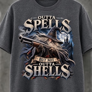 Puede incluir: Una camiseta gris oscuro con el gráfico de un mago con barba larga blanca y sombrero puntiagudo sosteniendo una escopeta de doble cañón. El texto dice OUTTA SPELLS BUT NOT OUTTA SHELLS, con cartuchos dispersos y un castillo al fondo.