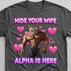 May include: A charcoal grey t-shirt featuring a graphic of a muscular cat with a human-like physique wearing dark jeans. The text "HIDE YOUR WIFE" and "ALPHA IS HERE" appears in purple and pink letters, surrounded by several floating pink hearts.