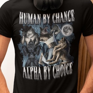 Pode incluir: Camiseta preta com um gráfico de três figuras semelhantes a lobos em um cenário de floresta. O texto "HUMAN BY CHANCE ALPHA BY CHOICE" é impresso em letras prateadas na camiseta.