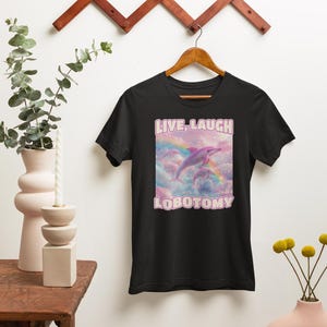 May include: Black t-shirt with a pink graphic of two dolphins jumping over a rainbow with the text "LIVE, LAUGH, LOBOTOMY" in pink.