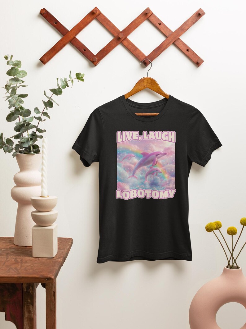 May include: Black t-shirt with a pink graphic of two dolphins jumping over a rainbow with the text "LIVE, LAUGH, LOBOTOMY" in pink.