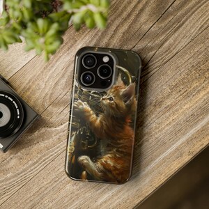 May include: A phone case with a brown tabby kitten playing on a gold musical instrument. The case has a camera lens cutout with three lenses.