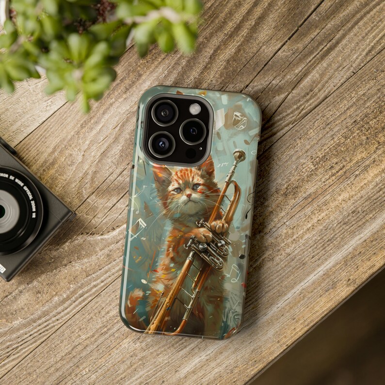 May include: A phone case with a colorful illustration of a cat playing a trumpet. The cat is orange and white with green eyes. The background is a light blue with musical notes and splashes of paint.