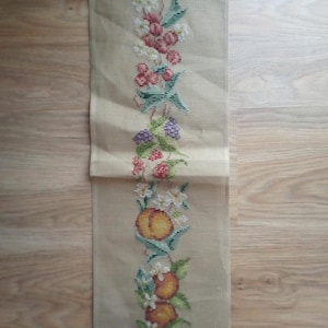 Könnte beinhalten: Eine beige Gobelin-Leinwand mit einem vertikalen Blumenmuster. Das gestickte Design zeigt Pfirsiche, Beeren und weiße Blüten mit grünen Blättern. Ein kleines Etikett ist angebracht. Maße in cm.