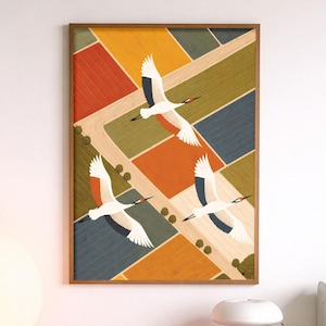 May include: A framed print depicting three white cranes soaring above a colourful patchwork landscape. The artwork hangs on a white wall above a pink shelf, which holds a spherical lamp and a stereo receiver. The print's frame is brown.