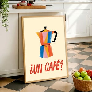 Puede incluir: Un cuadro enmarcado con una ilustración colorida de una cafetera italiana. La obra de arte está en un estilo moderno con formas geométricas en tonos naranja, rosa, azul y amarillo. El texto "¿UN CAFÉ?" está en rojo debajo.
