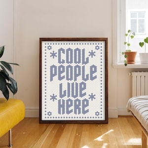May include: A rectangular framed wall art piece featuring a white background with a repeating hexagonal tile pattern. The text COOL PEOPLE LIVE HERE is displayed in a bold, blue, pixelated font, accented by small blue flower-like icons.