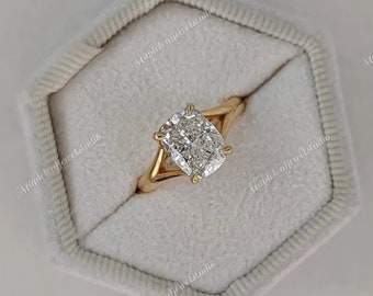 May include: A gold ring with a large, rectangular cushion-cut diamond. The diamond is held in place by four prongs, with a split shank design. The ring is displayed in a light grey velvet ring box.