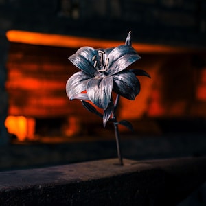 Può includere: Una scultura di fiore di giglio in metallo con finitura grigio scuro, in piedi su un'incudine nera.