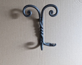 May include: A black metal hook with two decorative swirls at the top and a twisted stem. The hook is mounted on a brown cardboard background.
