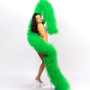 May include: A woman wearing a green feather boa and silver high heels. The boa is long and flowing, and the woman is posing with her arm raised.