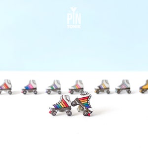 Könnte beinhalten: Regenbogen-Rollschuh-Ohrringe. Die Ohrringe sind aus Holz und mit einem Regenbogenmuster bemalt. Die Ohrringe sind auf einer weißen Oberfläche abgebildet.