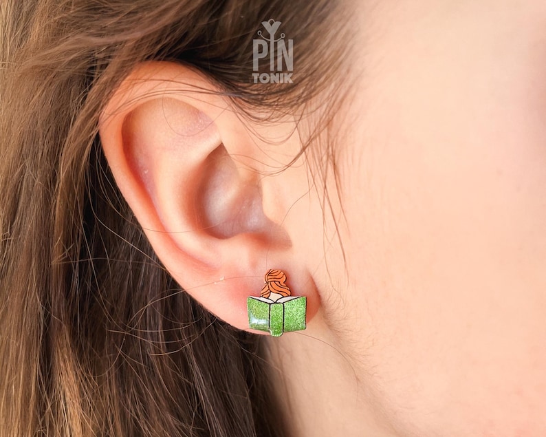 May include: A green book with a woman reading inside, a wooden earring.
