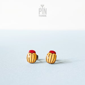 Può includere: Un paio di piccoli orecchini a forma di fiore di colore giallo e rosso. Gli orecchini sono in legno e hanno un design semplice e minimalista.