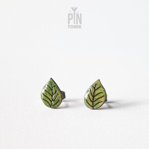 Pode incluir: Um par de brincos de botão de folha verde com contornos pretos. Os brincos são de metal e têm fecho de poste.