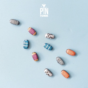 Peut inclure: Assortiment d'épingles ovales colorées avec différents motifs et designs. Les épingles sont sur un fond bleu clair.