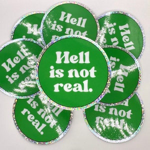 May include: A collection of green circular stickers with the phrase "Hell is not real" in white, bold font. Each sticker has a shimmering, silver border. The stickers are scattered across a white surface.