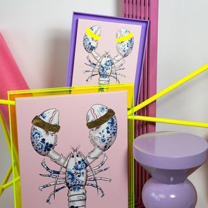 Peut inclure: Deux impressions encadrées d'un homard bleu et blanc avec des accents jaunes sur un fond rose. Les cadres sont jaune fluo et violet.