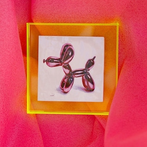 May include: A framed illustration of a pink balloon animal shaped like a dog. The illustration is on a white background and is framed in a yellow frame.