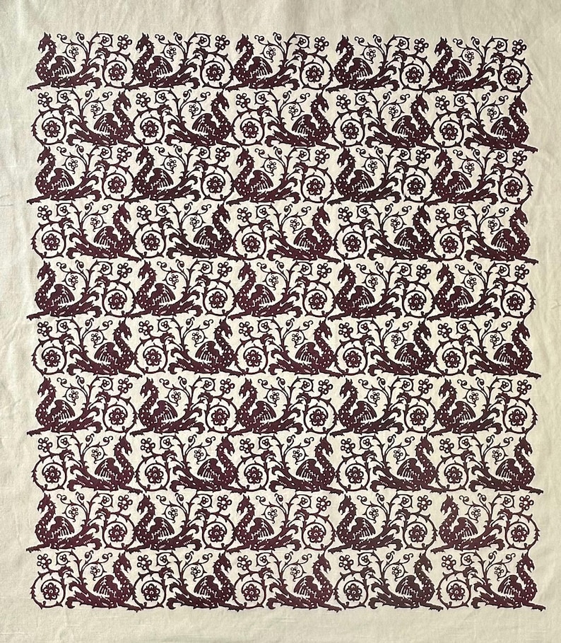May include: A cream-colored textile featuring a repeating pattern of stylized mythical creatures and floral elements in a deep burgundy hue. The design is symmetrical and covers the entire surface, creating a vintage aesthetic.