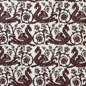 May include: Burgundy and cream-colored fabric with a repeating pattern of stylized dragons, floral elements, and scrolling vines. The design is reminiscent of medieval tapestries or heraldic motifs, creating a vintage or historical aesthetic.