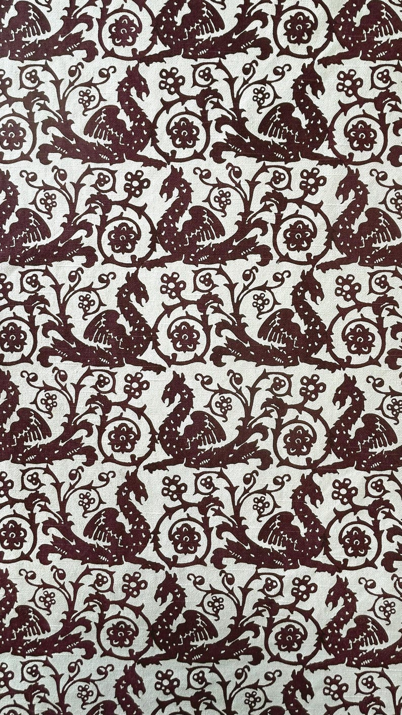 May include: Burgundy and cream-colored fabric with a repeating pattern of stylized dragons, floral elements, and scrolling vines. The design is reminiscent of medieval tapestries or heraldic motifs, creating a vintage or historical aesthetic.