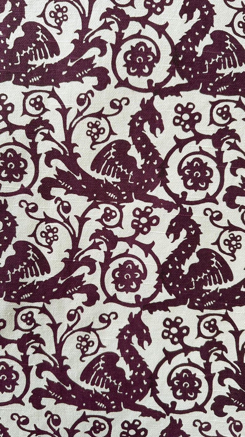 May include: Cream-colored fabric with a repeating pattern of stylized dragons, floral elements, and swirling vines in a deep burgundy color. The design has a vintage or medieval aesthetic, suitable for upholstery or decorative projects.