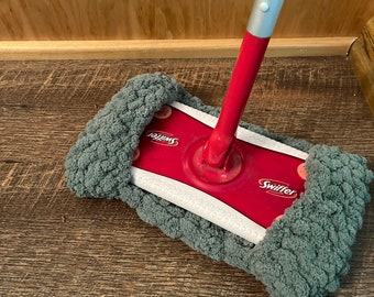 May include: A red and gray Swiffer sweeper with a gray microfiber pad is on a wood floor.