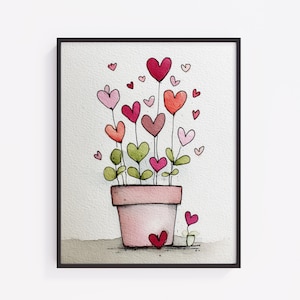 Puede incluir: Una impresión en acuarela enmarcada que presenta una maceta rosa con flores en forma de corazón en tonos rojos, rosas y verdes. Pequeños acentos de corazón flotan alrededor de las flores. La obra de arte está sobre un fondo blanco.