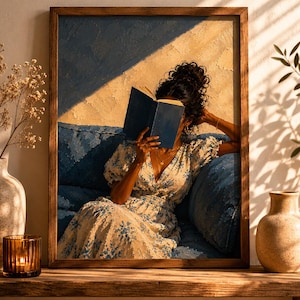 May include: A framed wall art print depicting a person with curly hair sitting on a blue sofa, reading a dark blue book. The person wears a white dress with a blue floral pattern. The scene features warm golden sunlight and deep blue shadows.