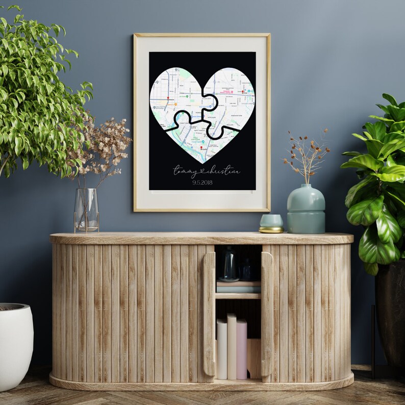 Puede incluir: Un mapa en blanco y negro de dos piezas de rompecabezas en forma de coraz&oacute;n con el texto "Tommy & Christine 9.5.2018" impreso debajo del coraz&oacute;n. El mapa est&aacute; enmarcado y colgado en una pared sobre un armario de madera.