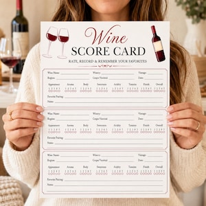 Puede incluir: Una tarjeta de puntuación de vino de papel blanco con el texto Wine SCORE CARD RATE, RECORD & REMEMBER YOUR FAVORITES. La tarjeta incluye ilustraciones de dos copas de vino y una botella, con tres secciones para registrar detalles.