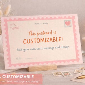 Puede incluir: Una postal personalizable con un borde rosa y el texto "This postcard is CUSTOMIZABLE!". La postal se muestra en un soporte de madera, con una vela encendida, sellos y un bolígrafo en el fondo. La postal te permite agregar tu propio texto, mensaje y diseño.