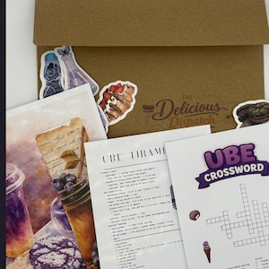 May include: A kraft paper envelope with stickers and printed recipe cards. Stickers include a butterfly, a beaker, and a pastry. Recipe cards feature text for Ube Tiramisu and an Ube crossword puzzle. The Delicious Dispatch logo is visible.