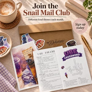 May include: A Snail Mail Club kit featuring a brown envelope labeled The Delicious Dispatch, a recipe card for Ube Tiramisu, an Ube crossword puzzle, and various food-themed stickers. A cup of coffee and a gold pen are placed nearby.