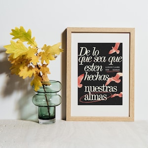 May include: A framed art print with the text "De lo que sea que esten hechas nuestras almas" in white script on a black background. The print features red bird illustrations and is in a light wood frame. A green glass vase holds yellow leaves.