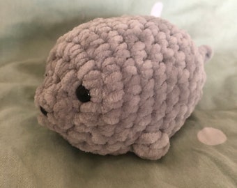 May include: A gray crocheted plush toy shaped like a seal. The seal has black eyes and a small, curled tail.