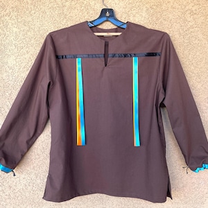 May include: A long-sleeved brown shirt with a keyhole neckline and decorative black ribbon across the chest. Vertical blue and orange ribbons are on the front. The cuffs and sleeve ends have blue trim.