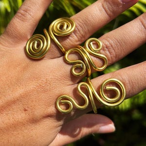 May include: Three gold rings with unique, abstract designs. The rings are made of twisted wire and are worn on a person's fingers.