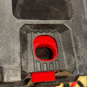 May include: A black plastic storage box with a red latch. The latch has a triangular warning symbol.