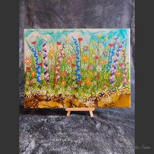 May include: A colourful painting of a field of wildflowers. The flowers are painted in shades of blue, purple, pink, red, yellow, and white. The background is a light blue sky with white clouds.