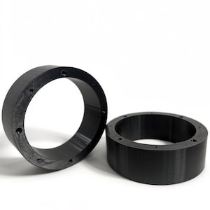 May include: Two black, circular objects with a series of evenly spaced holes. The objects have a cylindrical shape and appear to be made of a solid, dark material. The background is plain white, providing a stark contrast to the objects.